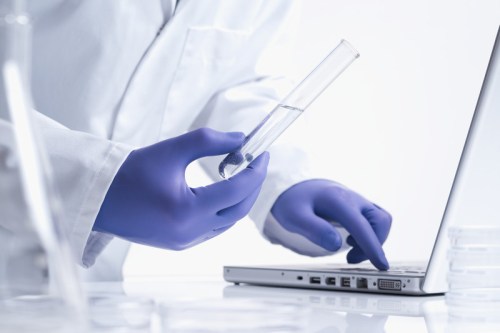 Photograph on person holding a test tube entering data into a laptop computer.